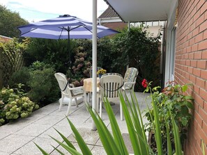 An outdoor patio with a table and chairs, surrounded by greenery and a brick wall. - Borkum Again (Borkum)