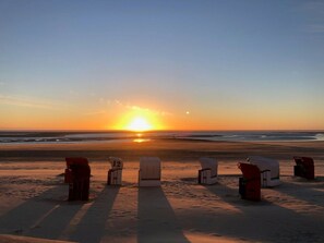 A beach with a row of beach huts aligned parallel to the shoreline, under a sunset sky. - Borkum Again (Borkum)