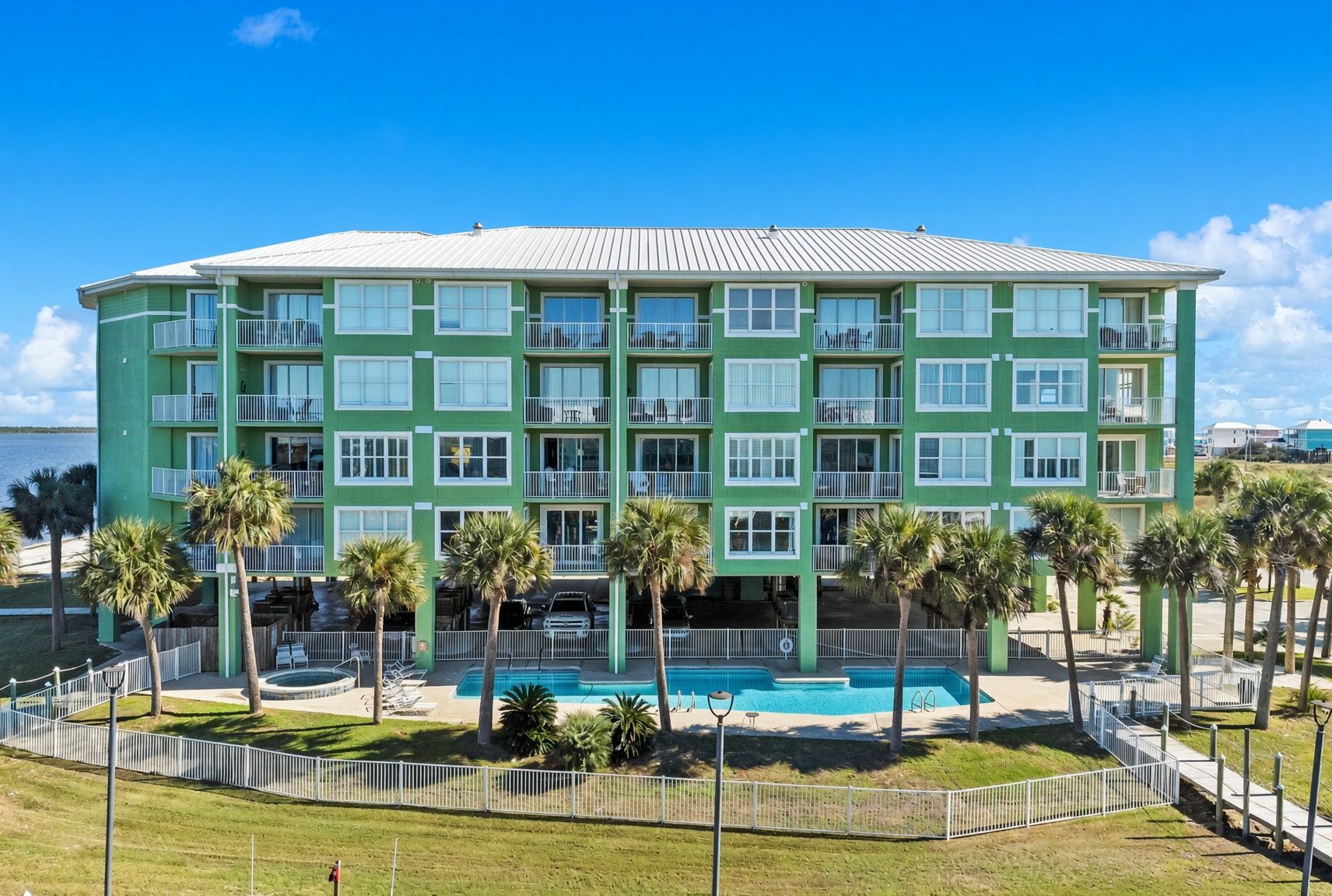 A multi-story hotel with a pool area, surrounded by palm trees and a fenced walkway.