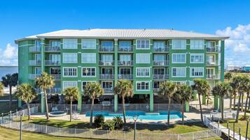 A multi-story hotel with a pool area, surrounded by palm trees and a fenced walkway.