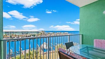 A balcony with a view of a marina and buildings, a glass table, and a chair.