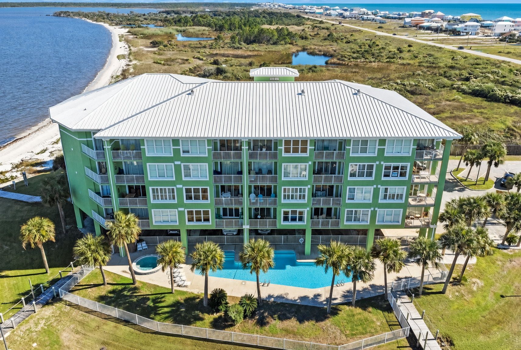 A multi-story hotel with a pool, surrounded by palm trees and a beach.