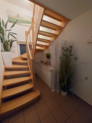 Una escalera de madera con techo de vidrio, una pared blanca con un cuadro y plantas en macetas.