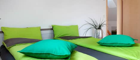 Un dormitorio con dos camas, cada una con ropa de cama verde y verde oscuro, una planta en maceta y una puerta de madera.