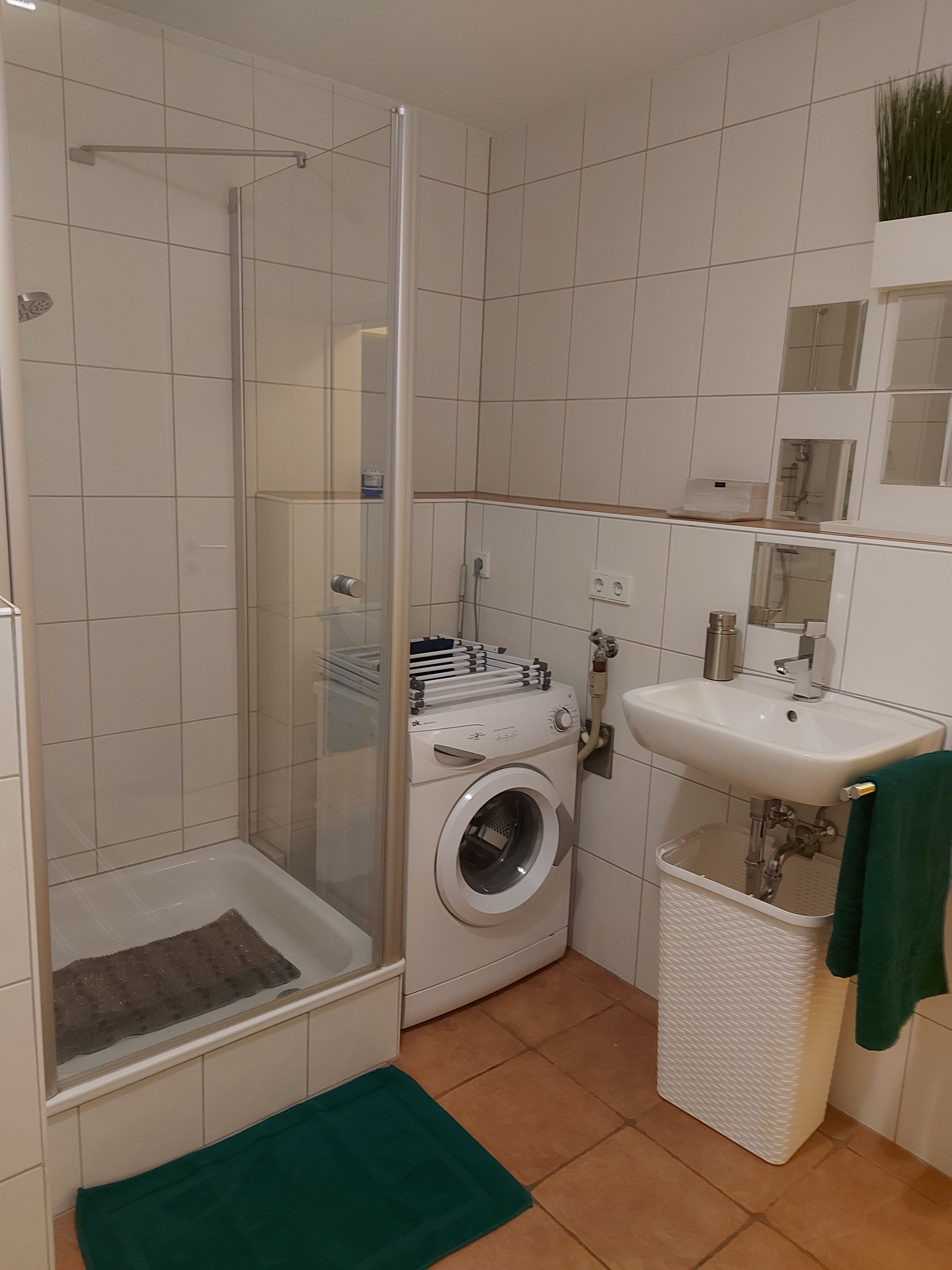 Ein kleines Badezimmer mit Duschkabine, Waschmaschine, Waschbecken und einem kleinen Mülleimer.