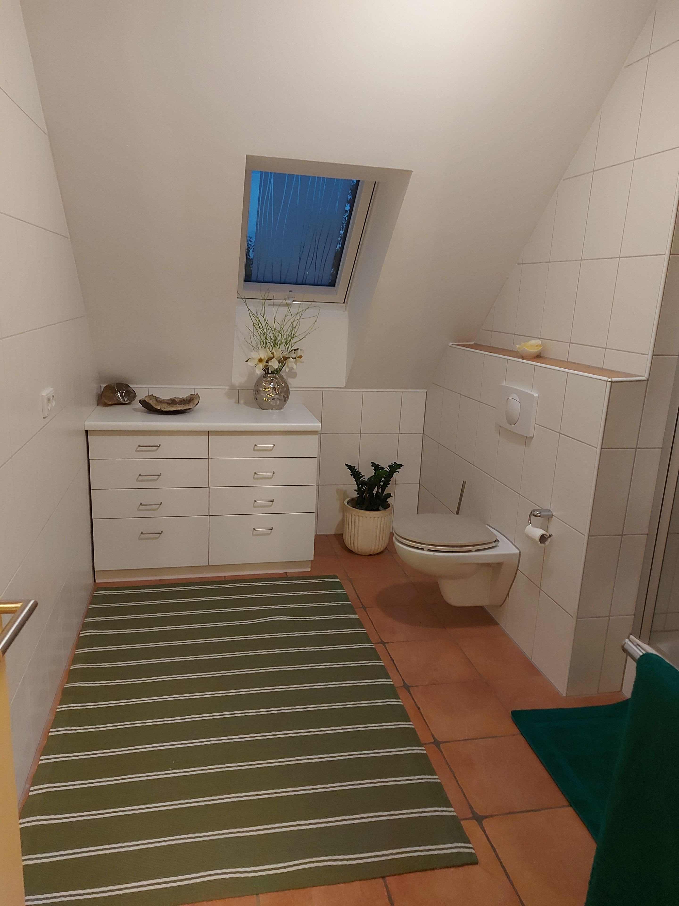 A small, modern bathroom with a toilet, sink, and a window above the sink.