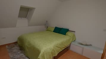 Ein Schlafzimmer mit einem Bett, einem Nachttisch, einer Lampe und einem kleinen Fenster.