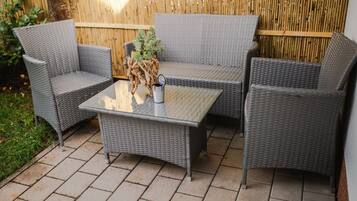 A wicker outdoor seating area with a glass table and chairs.