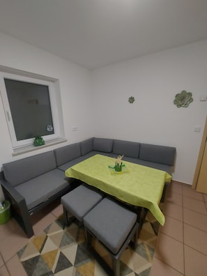 Una habitación de esquina con un sofá gris, una pequeña mesa con mantel verde y un suelo estampado.