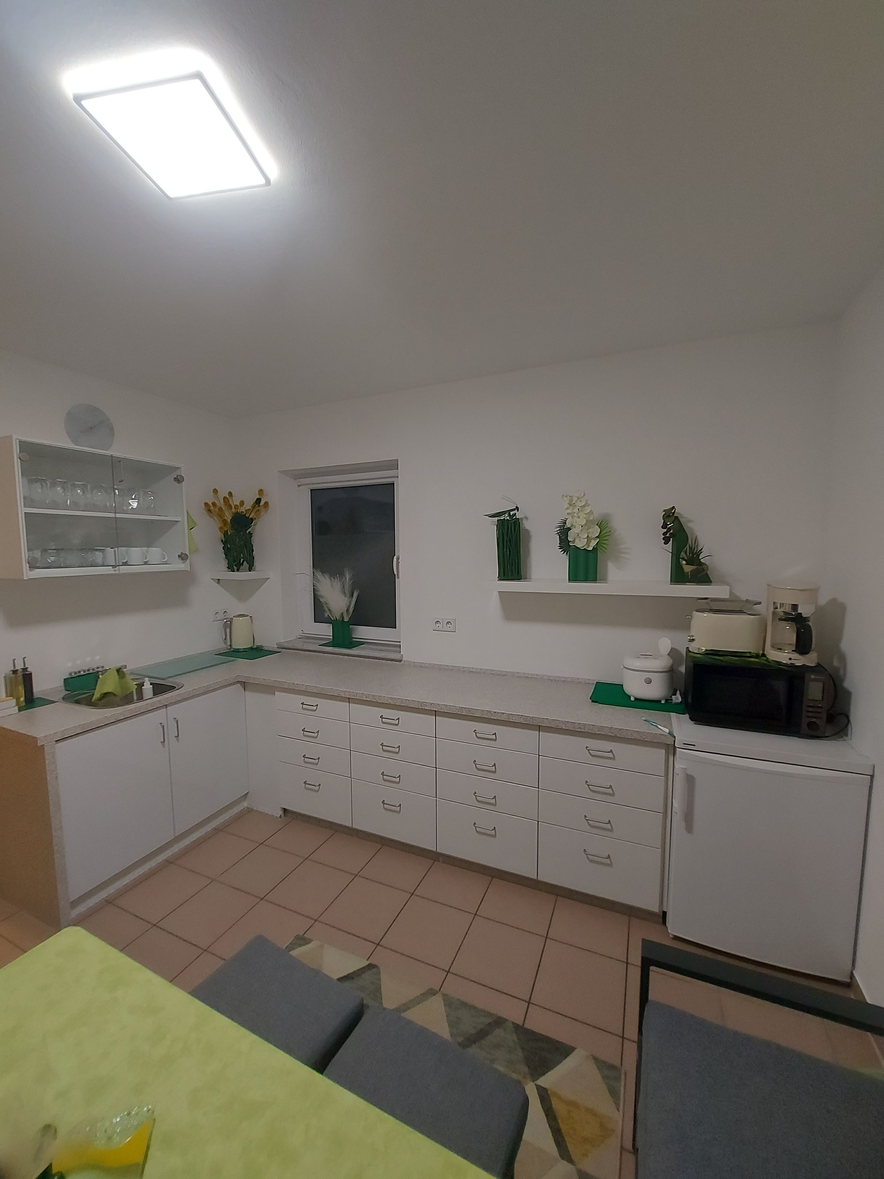 A modern kitchen with white cabinets, a microwave, a toaster, and a coffee maker. There is a window with a view of the outside.