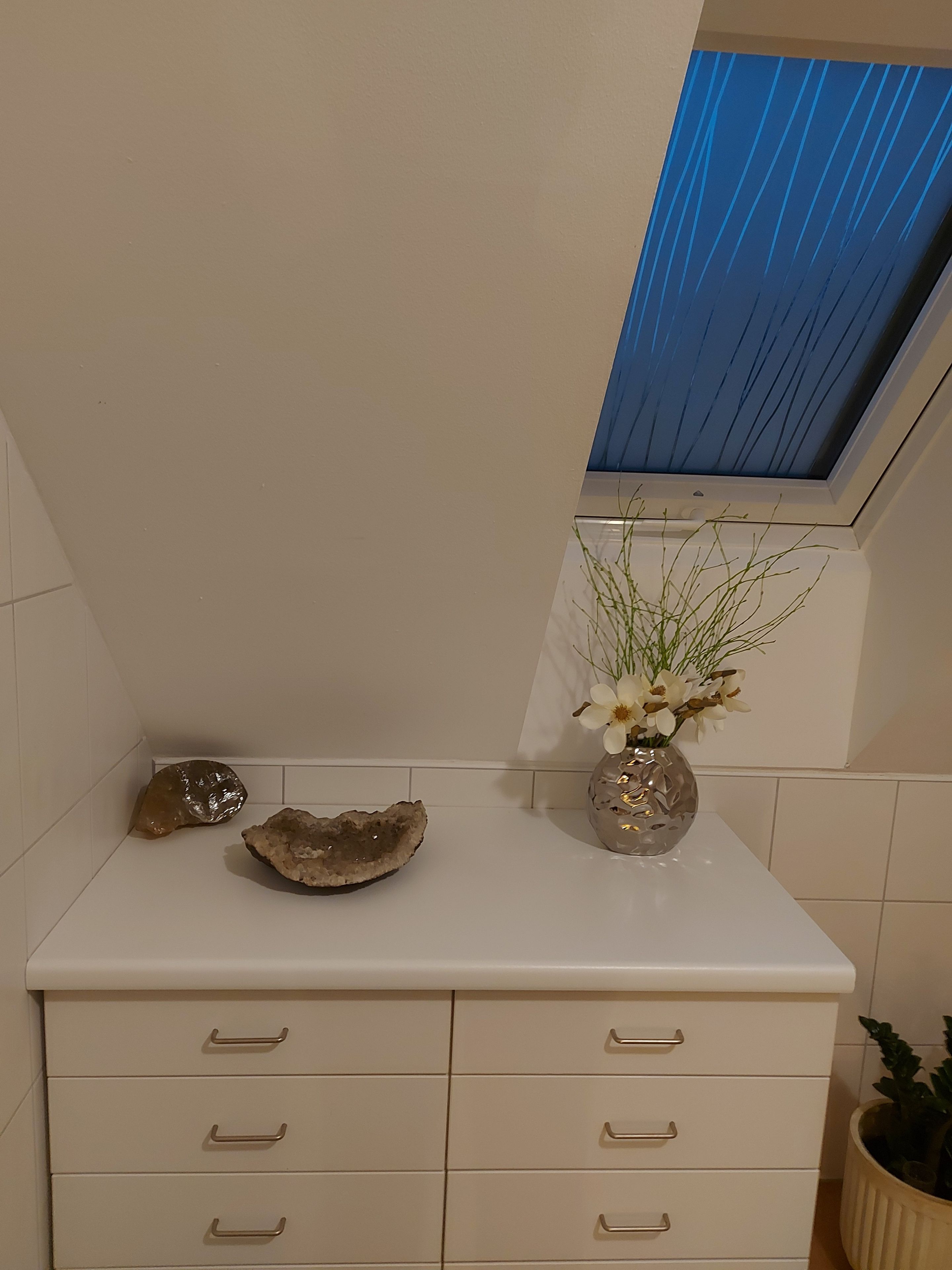 Un baño con tocador blanco, tragaluz y planta en maceta.