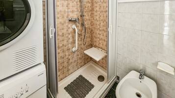 A bathroom with a shower, a toilet, and a washing machine.
