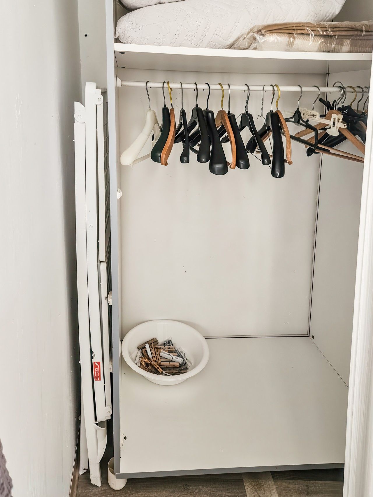 Ein weißer Schrank mit Kleiderstange und einer Schale Wäscheklammern.