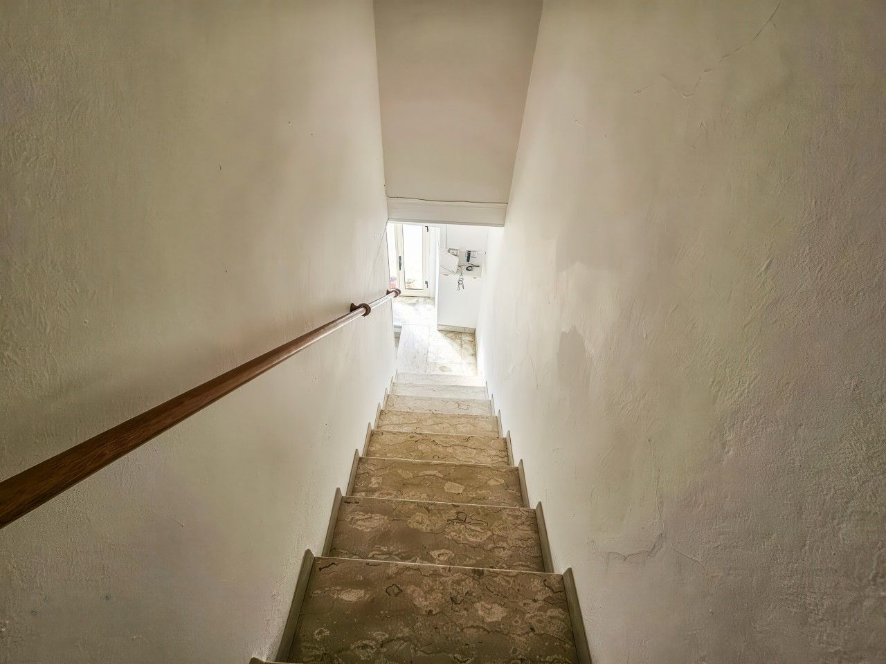 En smal trappe med gelænder i træ fører op til en døråbning.