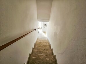 A narrow stairway with a wooden handrail leading to a doorway at the top.