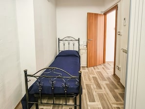 Un corridoio stretto con un letto, una porta in legno e una parete bianca.