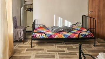 A single bed with a colorful quilt, a wooden wardrobe, and a chair with a cushion.