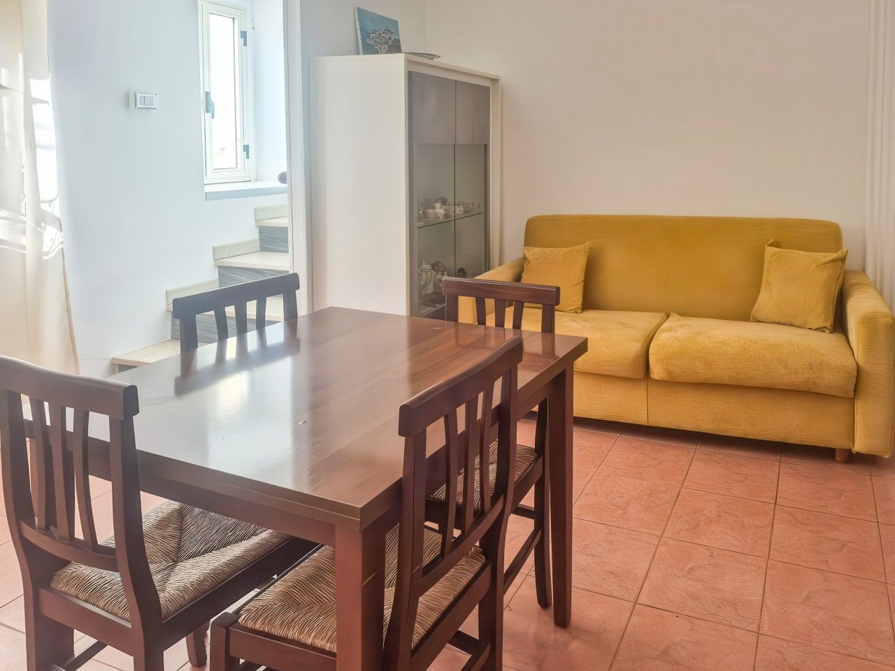 A dining area with a wooden table and chairs, a yellow sofa, and a cabinet.