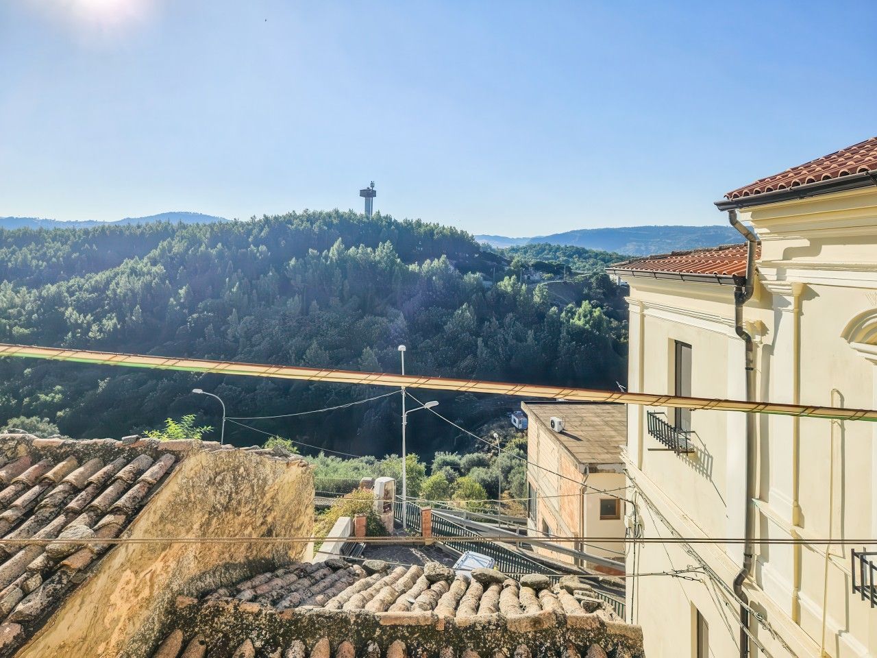 A view of a hillside with a building featuring a tiled roof and a balcony.