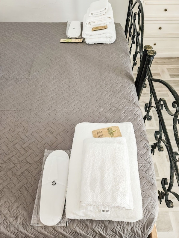A neatly made bed with a grey quilt, a white pillow, and a folded white towel with a tag.