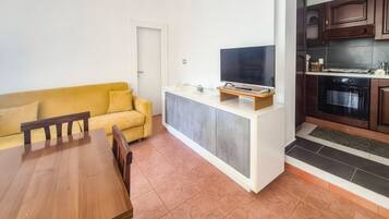 Ein kompakter Wohnraum mit Esstisch, gelbem Sofa, Küchenzeile und Flachbildfernseher.