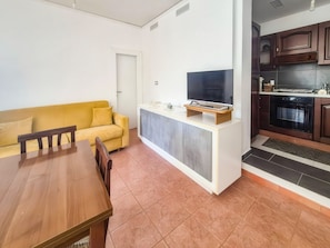 A compact living space with a dining table, yellow sofa, kitchenette, and a flat-screen TV.