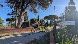 Dos ciclistas en un camino de grava, con un cartel de 'Casa Rurale' en primer plano.