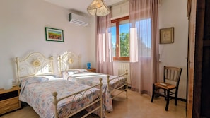 Una camera da letto con due letti, una finestra con tende, una sedia e un comodino.