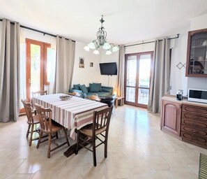Ein Essbereich mit Tisch und Stühlen, einer Couch, einem Fernseher und einer Küchenzeile mit Schränken.