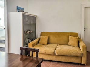A living room with a sofa, a dining table, and a cabinet with glass doors.