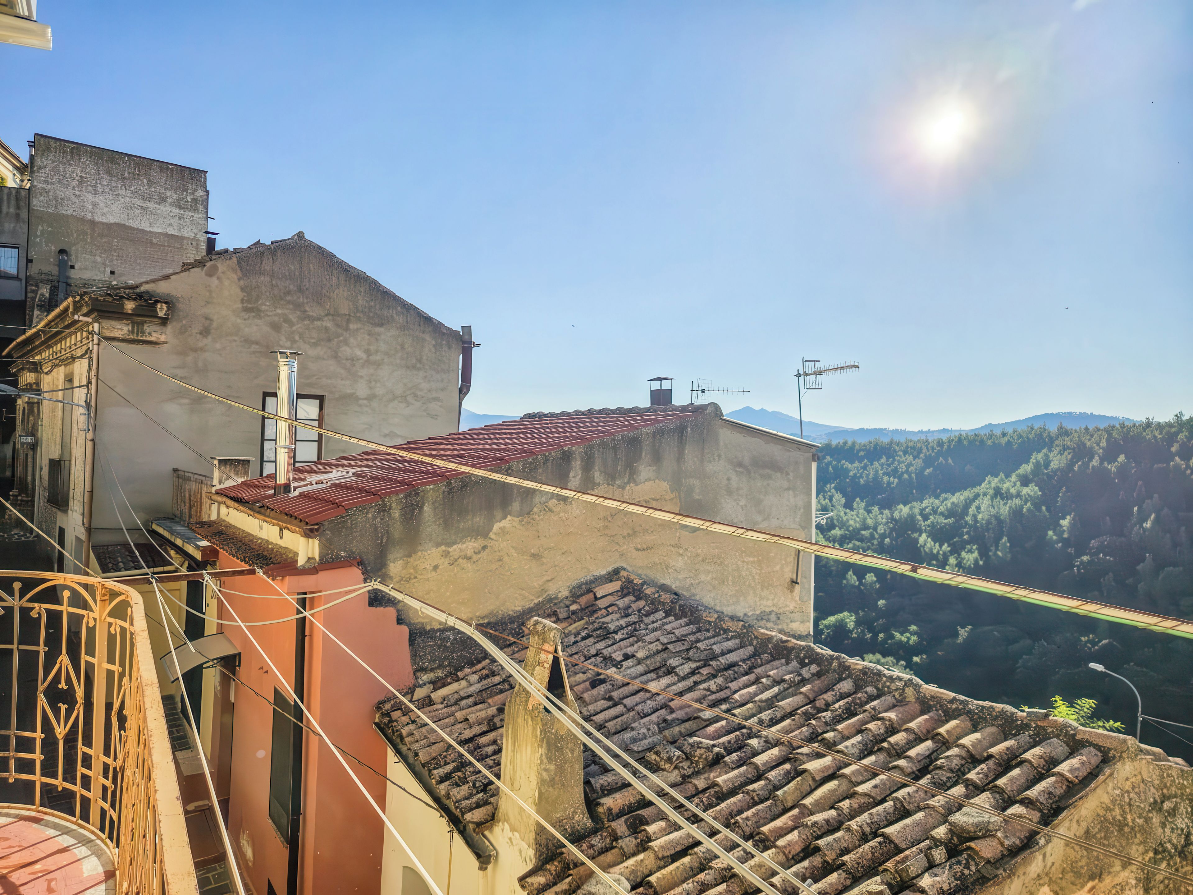 Un toit-terrasse avec une toiture recouverte de tuiles rouges, un escalier et une vue sur une chaîne de montagnes boisées.