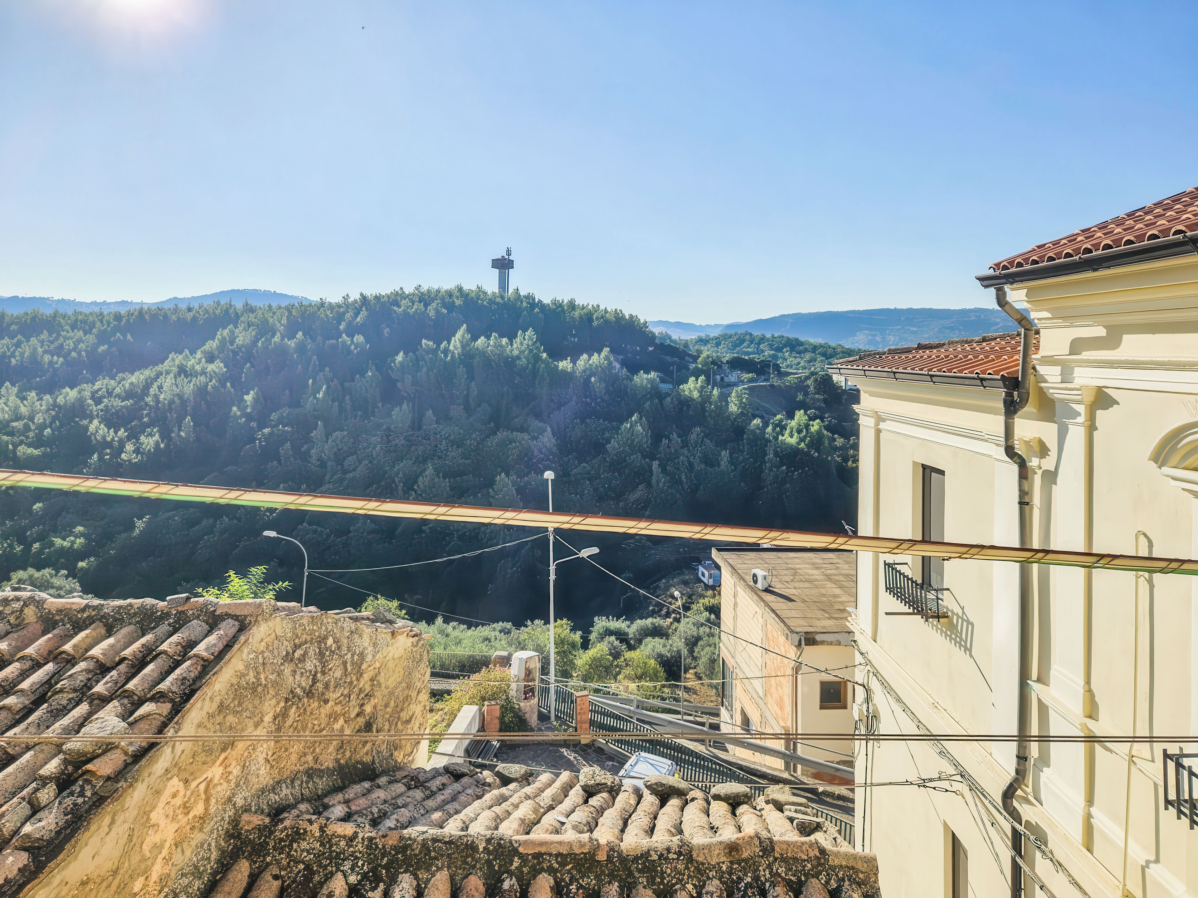 A view of a building with a tiled roof, a balcony, and a mountainous landscape in the background.