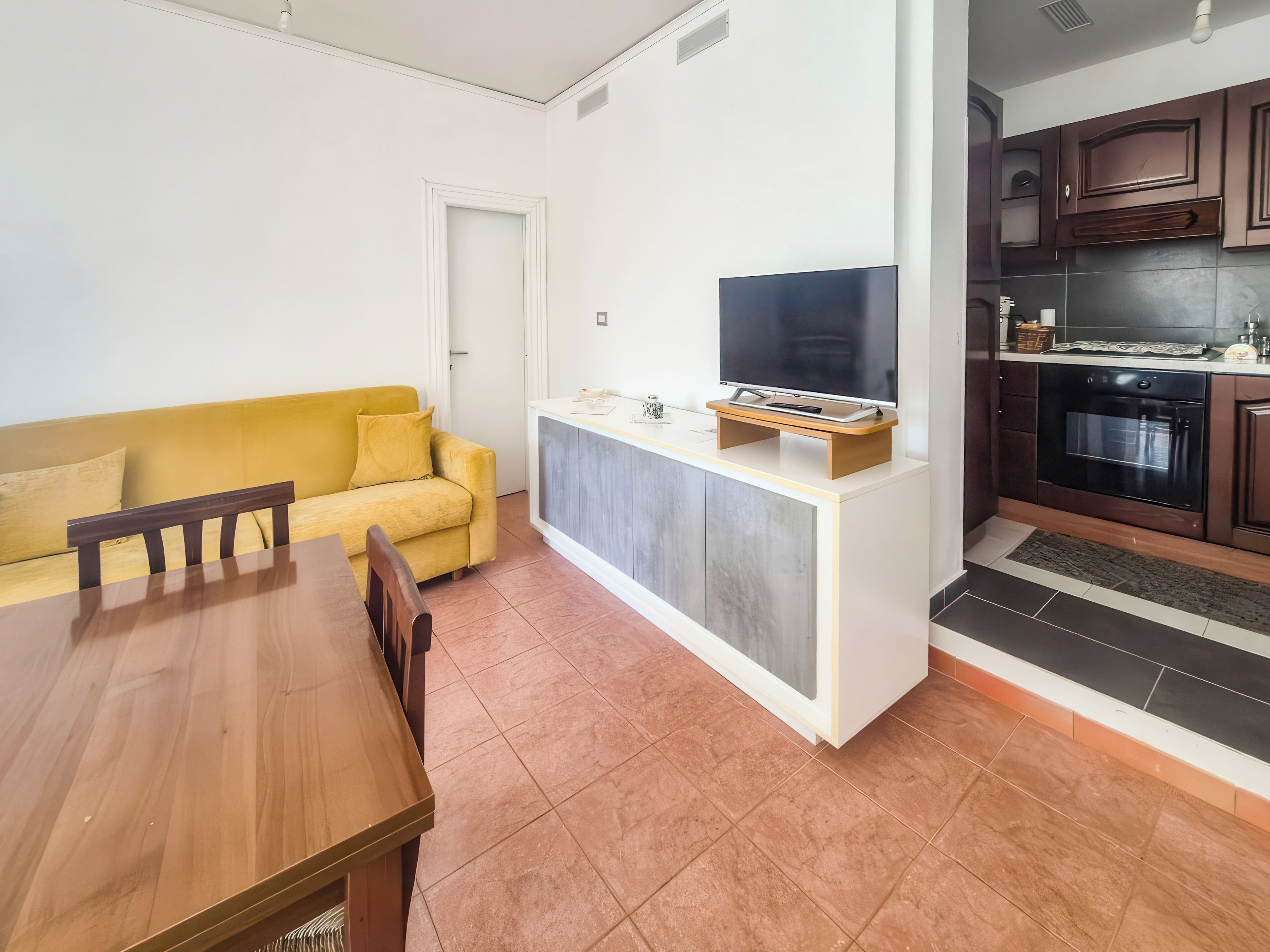 Un espacio habitable compacto con sofá, mesa de comedor, kitchenette y televisor.
