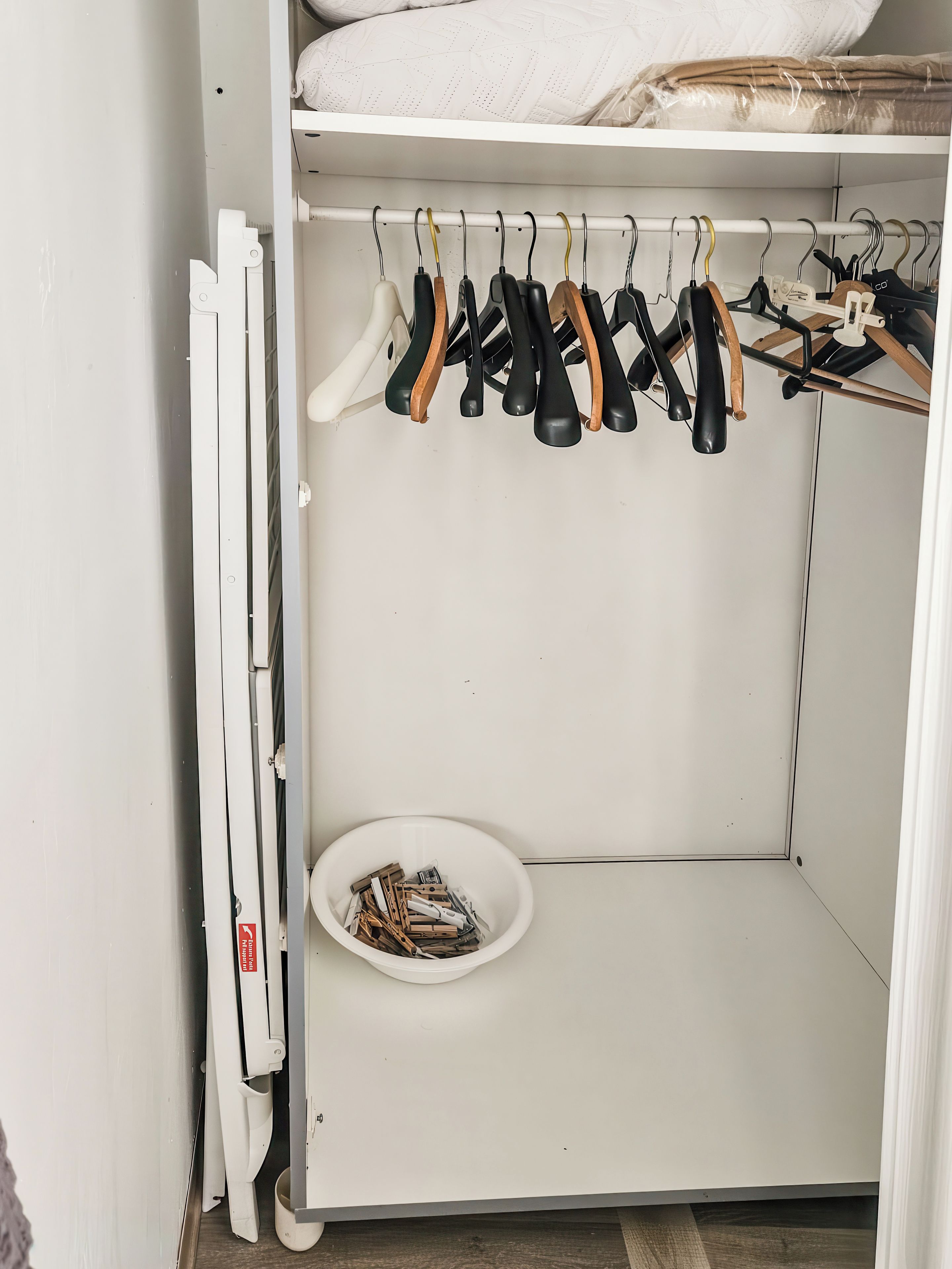 Un armario blanco con barra para colgar ropa y un bol con productos de limpieza.