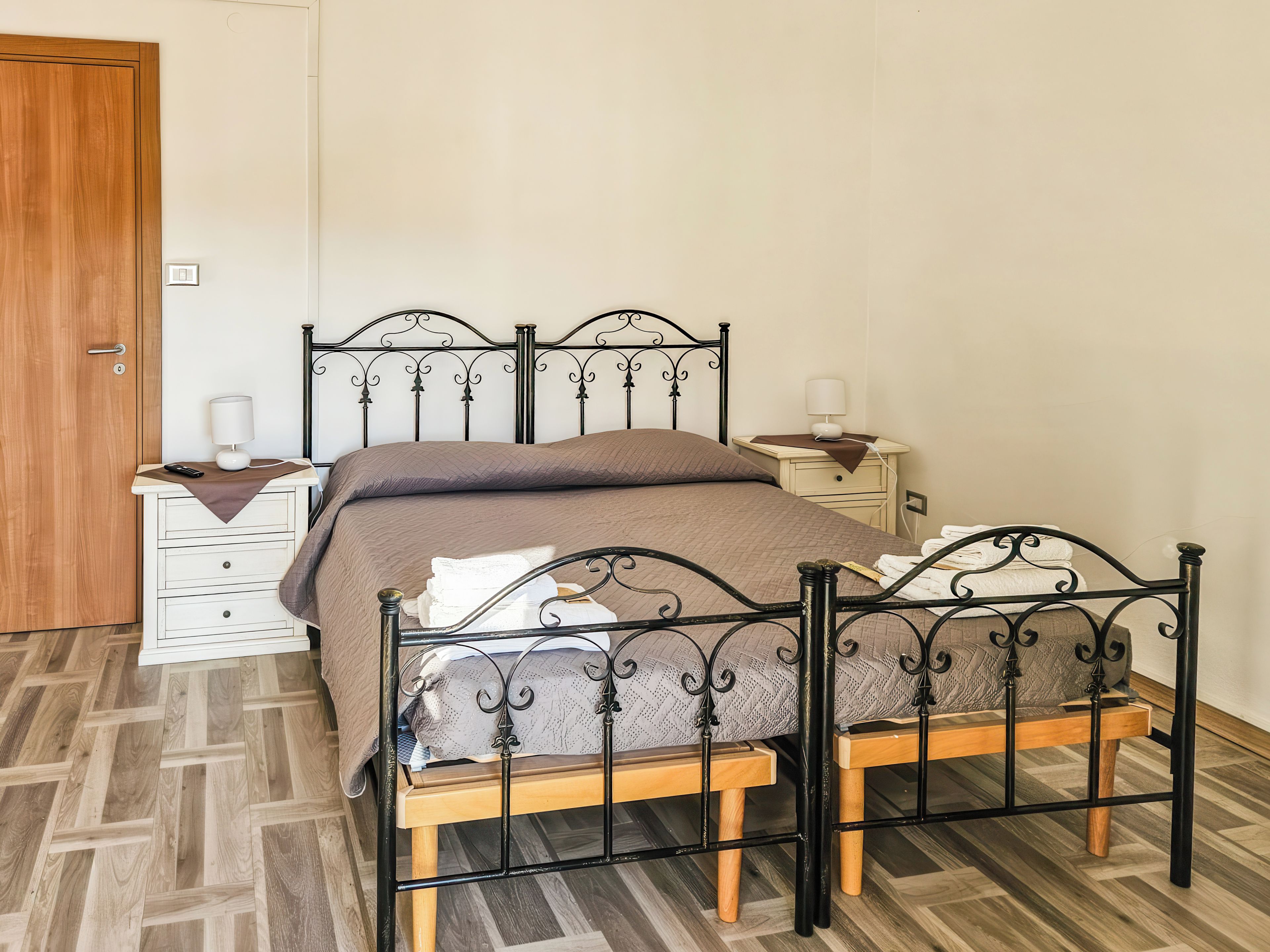 A room with a bed, bedside tables, a wooden door, and a patterned floor.