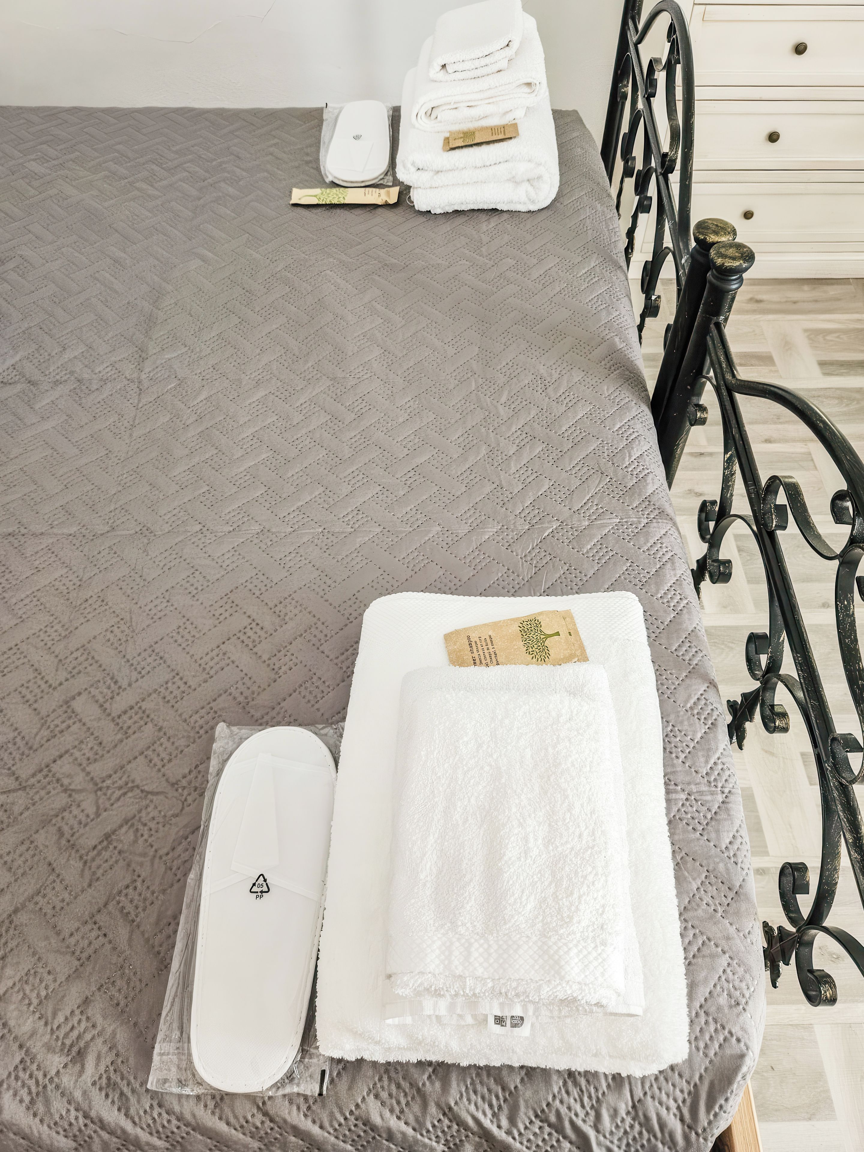 Un letto rifatto con cura, un copriletto grigio, un cuscino bianco e un asciugamano piegato di colore bianco con un'etichetta.