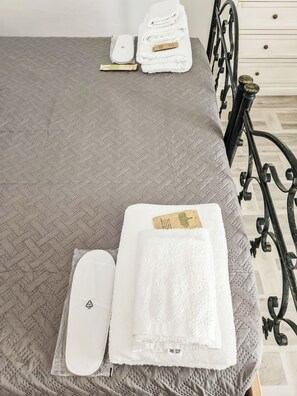 Una cama bien hecha con colcha gris, almohada blanca y toalla blanca doblada con una etiqueta.