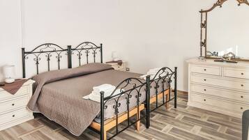 A neatly arranged bedroom with a metal bed frame, a bedside table with a lamp, a dresser with drawers, and a mirror on the wall.