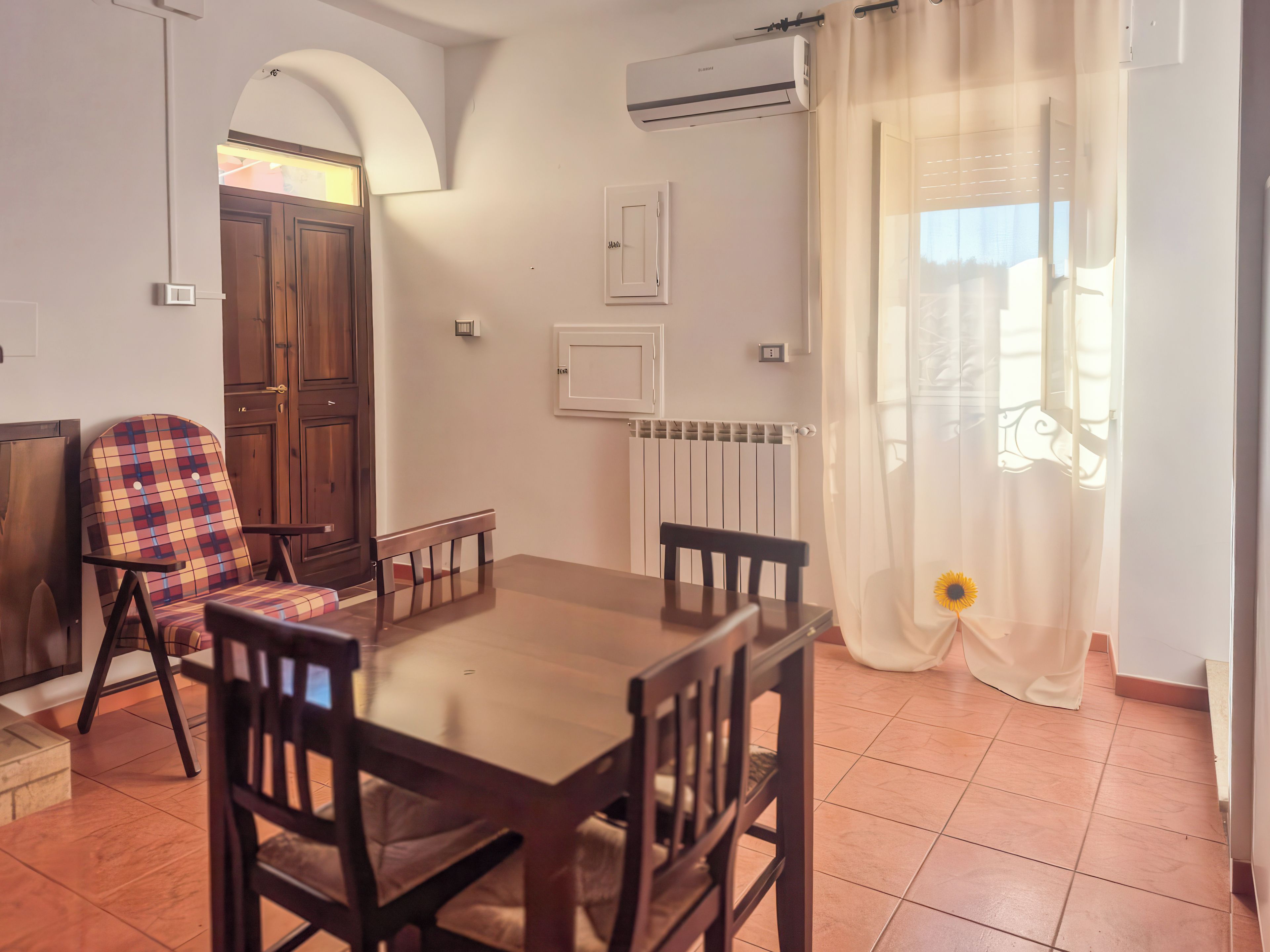 Un'area pranzo con un tavolo e sedie in legno, un termosifone e una finestra con tende.