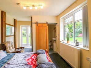 A bedroom with a bed, a window with a view of greenery, a bathroom with a toilet and sink, and a wooden door. - Greystones-a (Buxton)