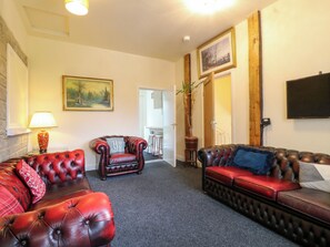 A living room with leather sofas, a lamp, a painting, and a potted plant. - Greystones-a (Buxton)