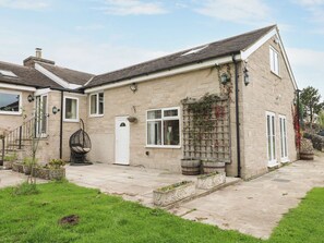 A stone building with a tiled roof, a hanging chair, and a door with a small garden. - Greystones-a (Buxton)