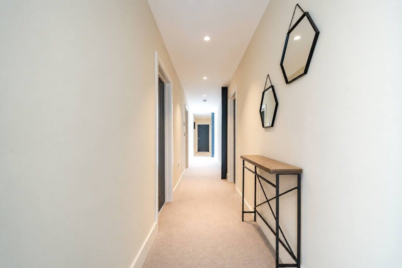 A corridor with a carpeted floor, a wooden console table, and two wall-mounted mirrors.