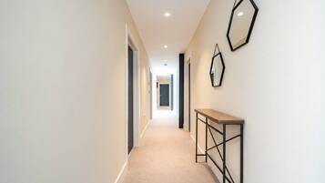 A corridor with a carpeted floor, a wooden console table, and two wall-mounted mirrors.