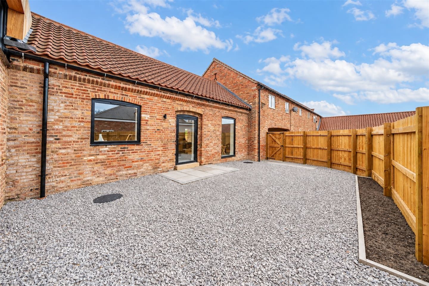 Een gebouw van baksteen met een grindpad en een houten omheining.