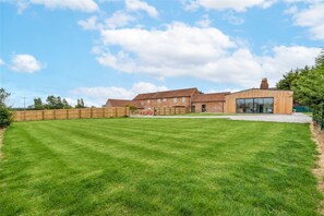 A spacious lawn with a wooden fence, a brick building, and a modern structure with large windows.