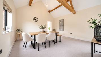 A dining area with a wooden table, four chairs, a clock, and a plant on the windowsill.