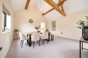A dining area with a wooden table, four chairs, a clock, and a plant on the windowsill.