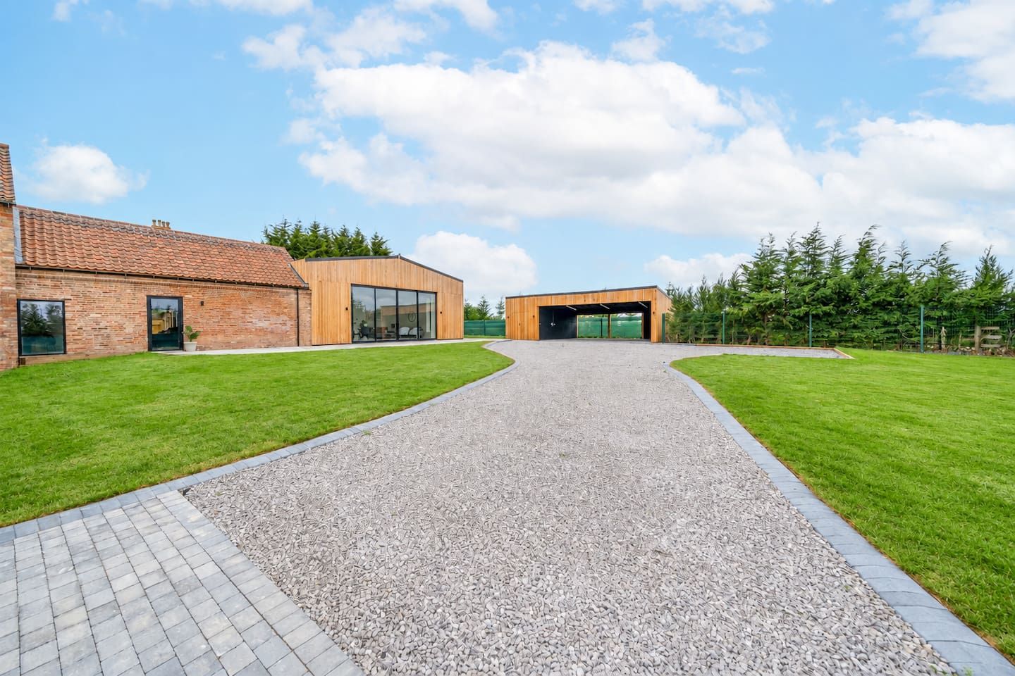 A building with a gravel driveway leading to a modern entrance, surrounded by well-maintained grass and trees.