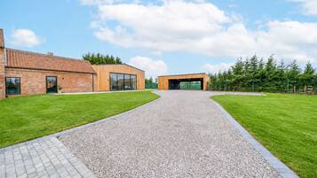 A building with a gravel driveway leading to a modern entrance, surrounded by well-maintained grass and trees.